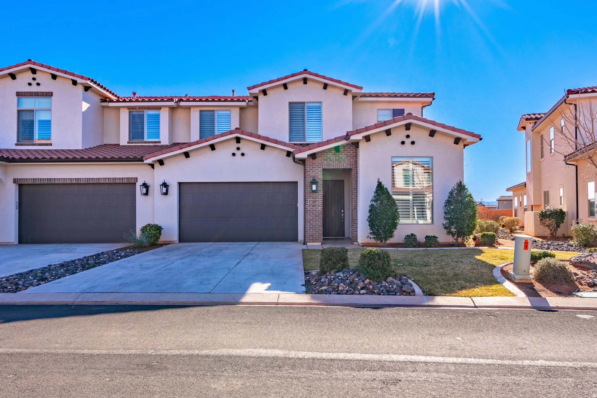 Stucco exterior with a tiled roof, integrated two-car garage, and a landscaped front yard featuring rock detailing
