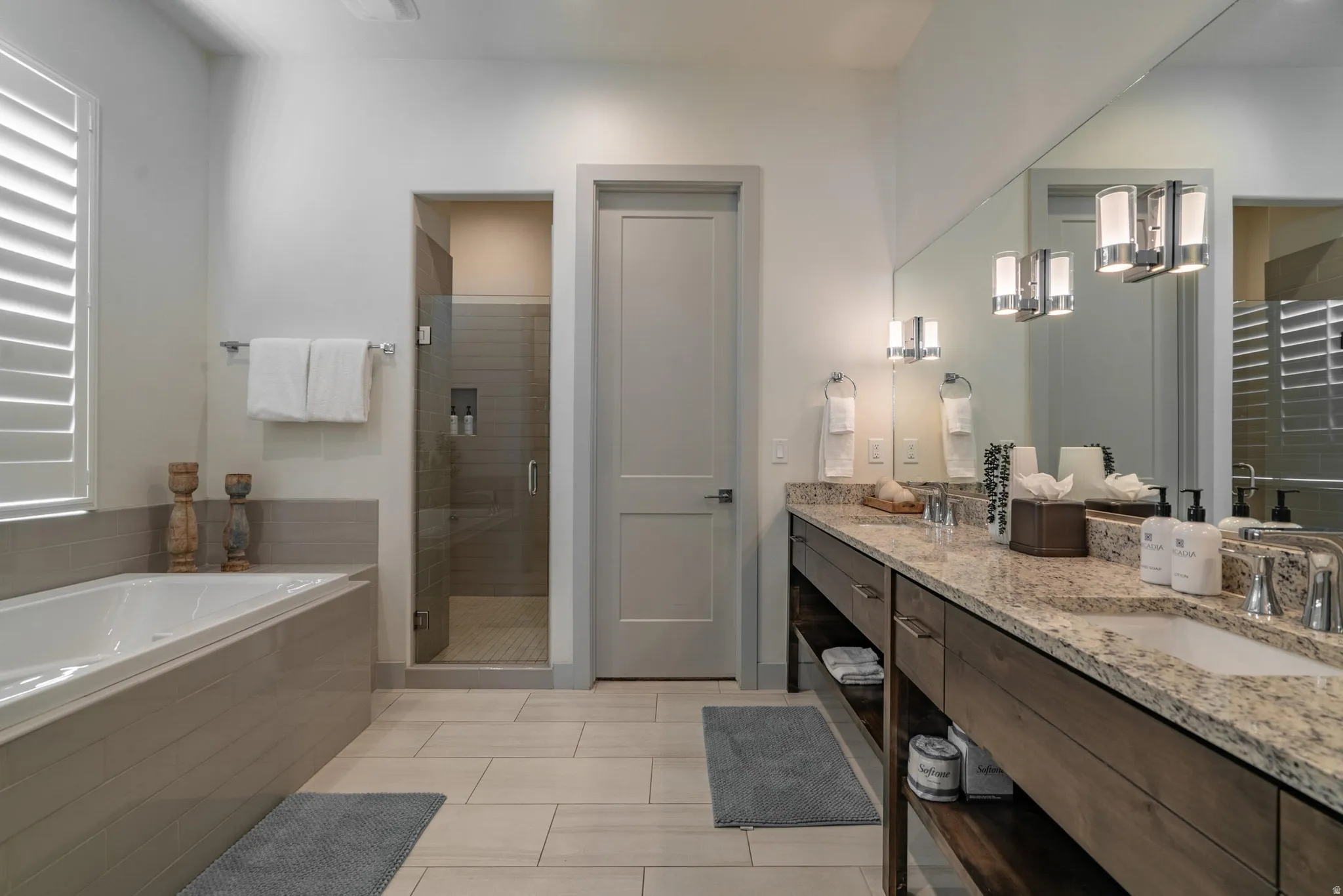 Main Floor Primary Ensuite Dual vanity with granite countertop, integrated soaking tub, separate glass-enclosed shower, wood-finish cabinetry, and neutral tile flooring