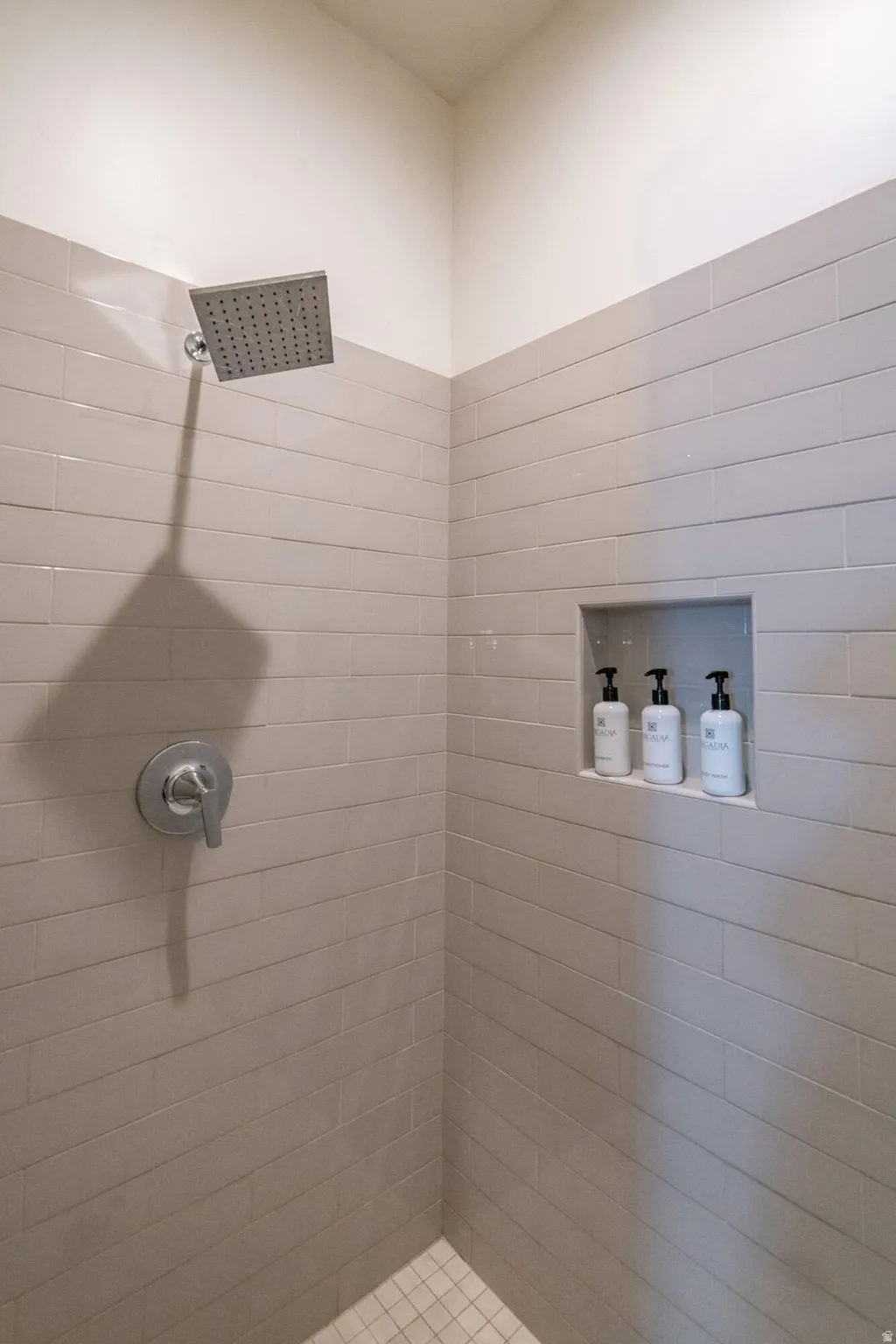 Main Floor Primary Ensuite Shower featuring gray horizontal tile, a recessed niche, a rainfall showerhead, and a chrome single-handle control