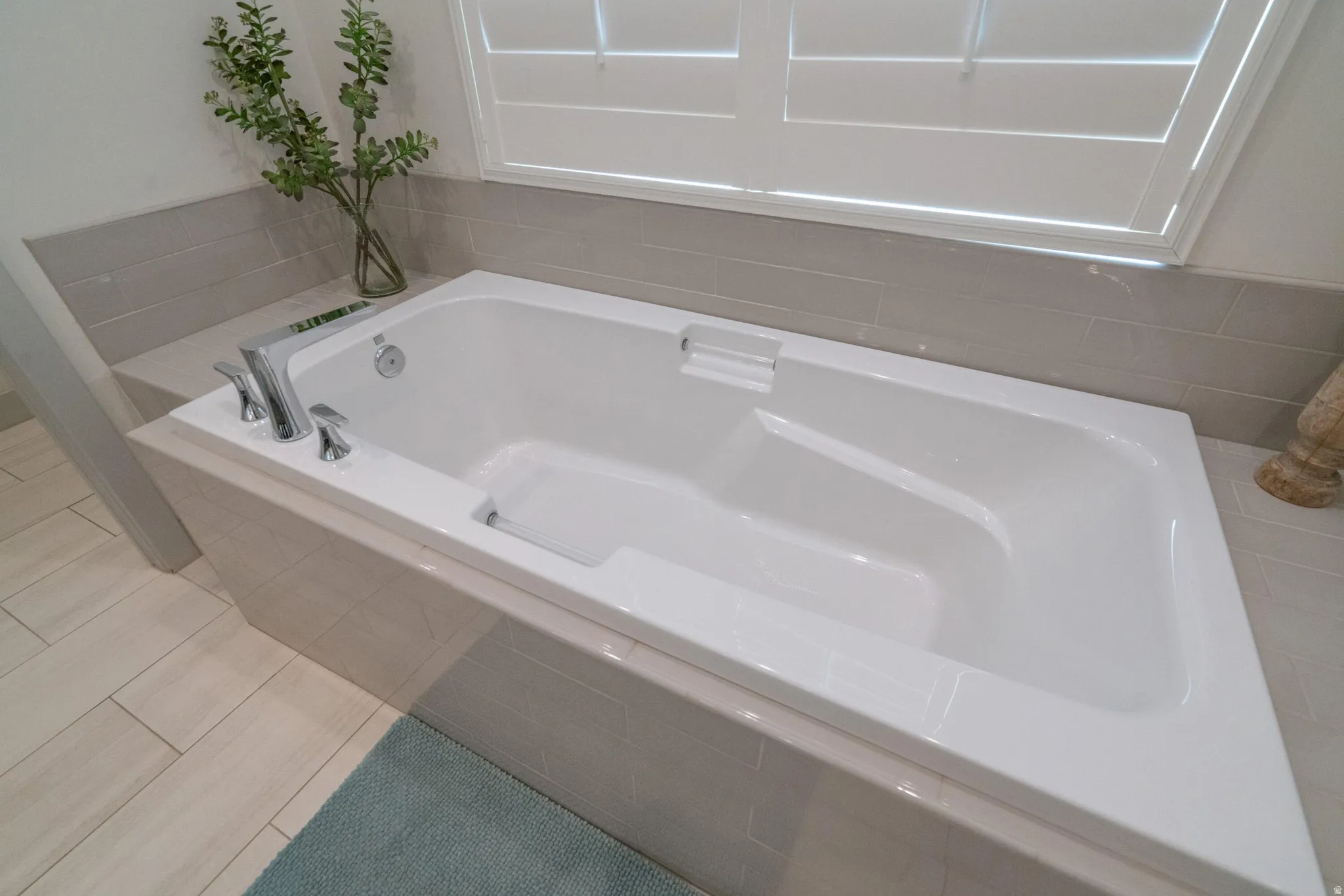 Main Floor Primary Ensuite Built-in soaking tub with chrome fixtures, surrounded by horizontal tile detailing and wood-finish flooring