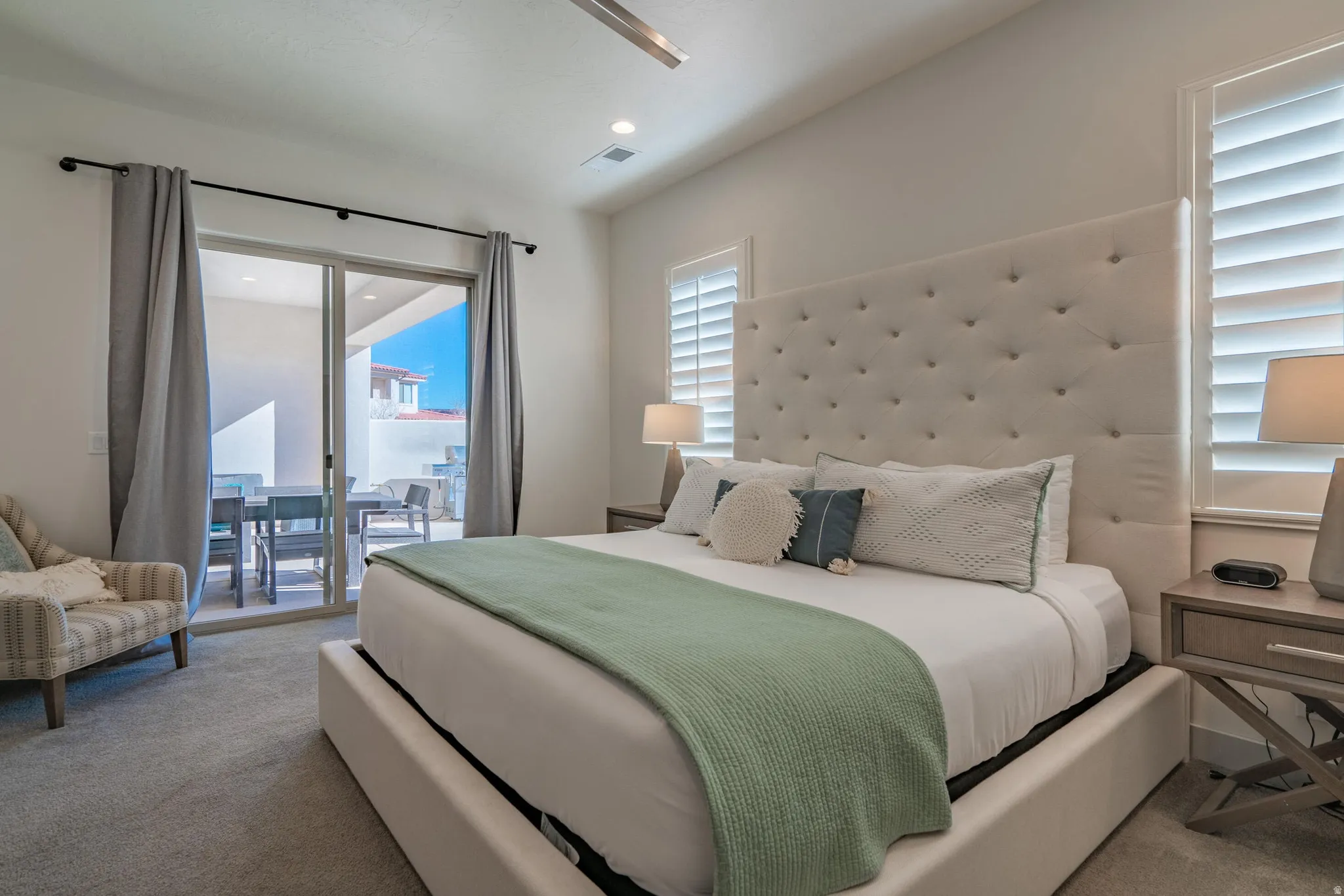 Main Floor Primary Bedroom with recessed lighting, ceiling fan, sliding glass door to outdoor patio, white plantation shutters, and light colored carpeting