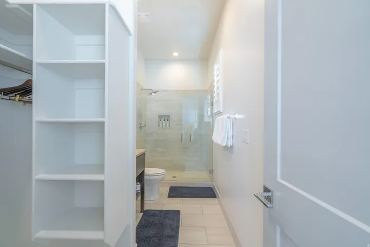 Main Floor Bedroom 2 Ensuite with Built-in shelving and closet rod, walk-in shower with glass enclosure, recessed shower niche, and louvered window
