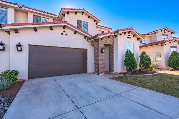 Stucco exterior with a tile roof, an integrated garage, brick entry accents, and mature landscaping