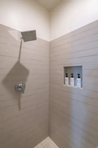 Main Floor Primary Ensuite Shower featuring gray horizontal tile, a recessed niche, a rainfall showerhead, and a chrome single-handle control