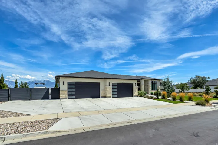 Contemporary architecture featuring a light-toned exterior, dark-toned garage doors with frosted glass panels, and a well-maintained front yard with varied landscaping