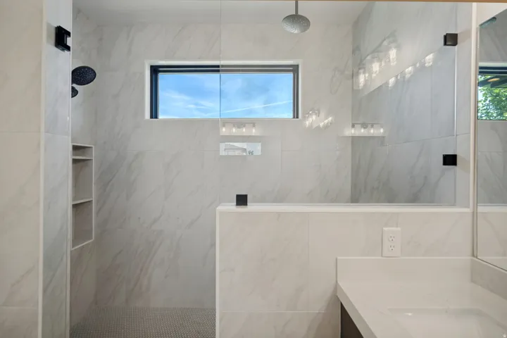 Walk-in shower with rain head and handheld shower fixtures, integrated shelving, and glass enclosure