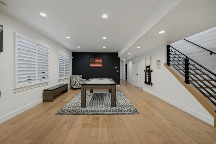 Expansive entertainment space featuring light wood-finish flooring, recessed lighting, and white plantation shutters