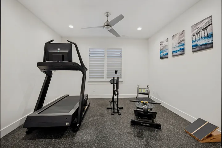 Recessed lighting, ceiling fan, window with plantation shutters, rubberized flooring, and bright white walls
