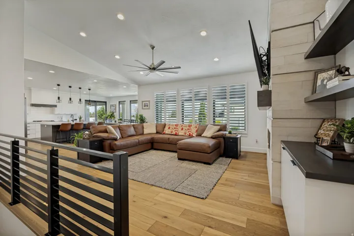 Vaulted ceiling with recessed lighting, wood-finish flooring, plantation shutters, and a built-in media cabinet with floating shelves
