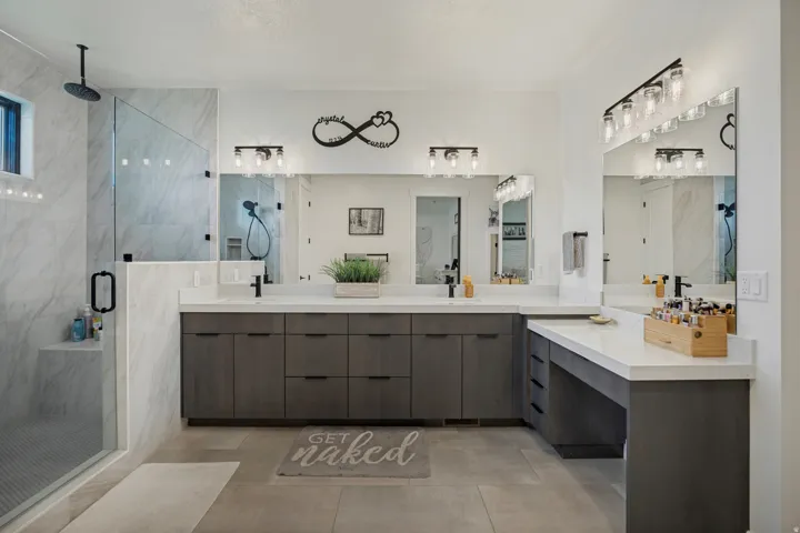 Spacious bathroom featuring a glass-enclosed shower with a rain shower head, dual vanities with integrated sinks, and a built-in makeup counter