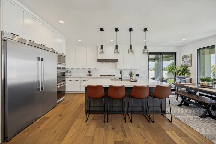Kitchen featuring stainless steel appliances, white cabinetry, a central island with countertop seating, wood-finish flooring, and pendant lighting