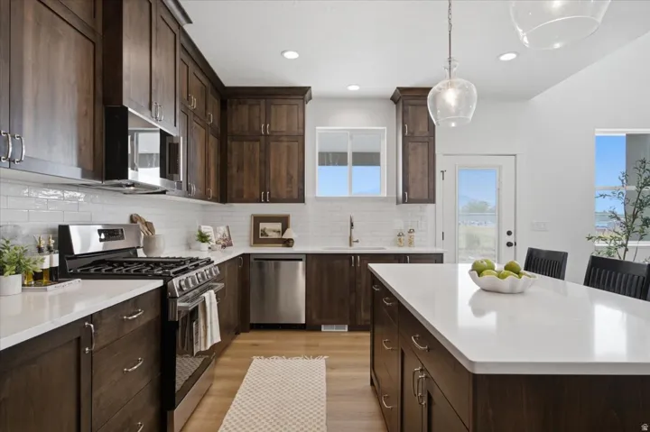 Dark wood-finish cabinetry, white subway tile backsplash, stainless steel appliances, white countertops, and wood-finish flooring