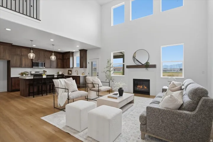 Spacious open-concept living area with soaring ceilings, wood-finish flooring, a built-in fireplace, and a kitchen featuring dark wood cabinetry and stainless steel appliances