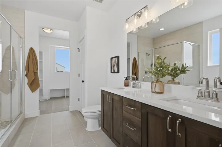 Dual vanity with white countertops and dark wood-finish cabinetry, frameless glass shower enclosure, and tiled flooring