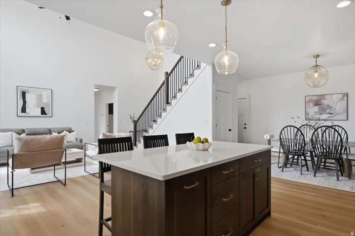 Vaulted ceiling, open-concept living space, wood-finish flooring, central island with solid surface countertop, and staircase with dark wood handrail