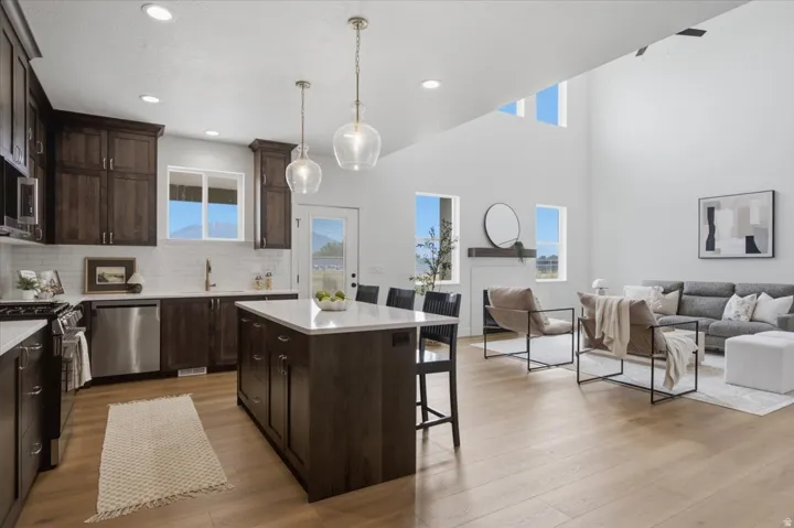Open-concept living area with wood-finish flooring, vaulted ceilings, and a kitchen featuring dark wood cabinetry, white countertops, and stainless steel appliances