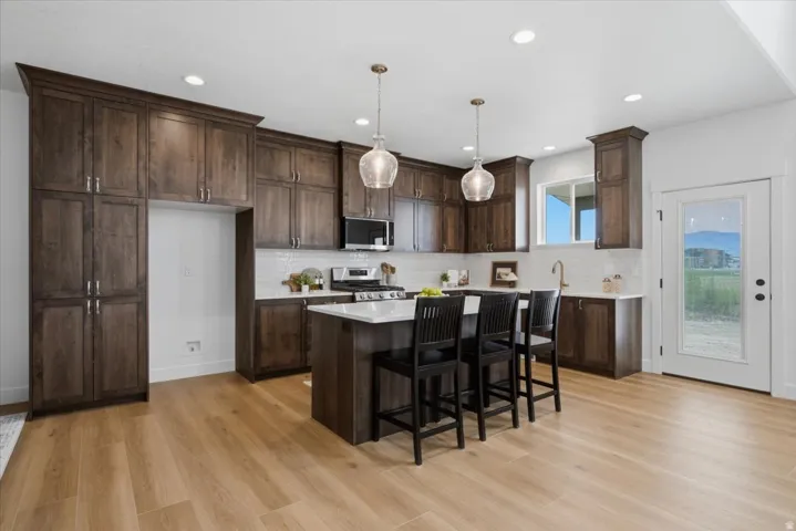 Spacious kitchen featuring extensive dark wood cabinetry, a central island with countertop seating, wood-finish flooring, a subway tile backsplash, and a glass-paned exterior door