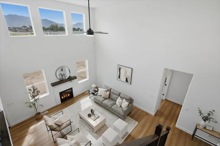Two-story ceiling, gas fireplace with wood mantel, wood-finish flooring, multiple windows, and a ceiling fan
