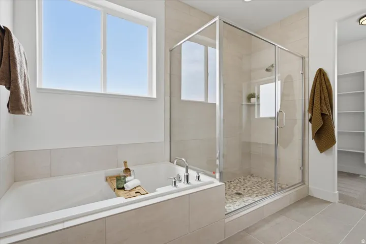 Soaking tub with chrome fixtures, tiled surround, and a clear glass enclosed shower with pebble flooring