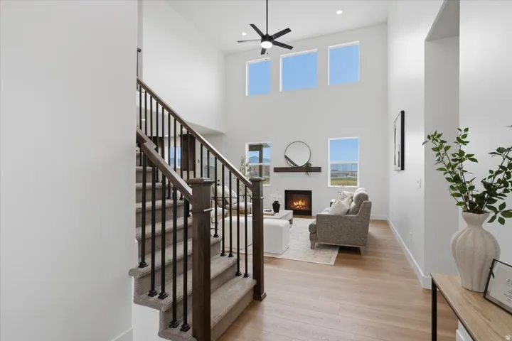 Two-story entry with wood-finish flooring, a carpeted staircase with wrought iron balusters, a ceiling fan, and a fireplace with a mantel