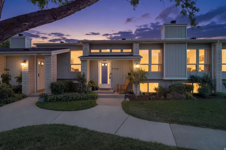 Modern architectural facade featuring brick and siding accents, multiple large windows, and a prominent front entry with a blue door