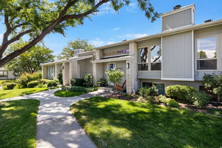 Light gray exterior with white trim, brick accents, multiple windows, and a paved walkway