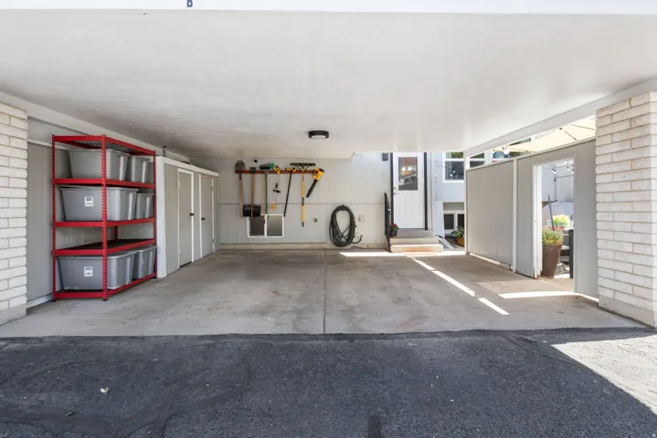 Covered carport with a concrete slab, integrated storage units, and brick-clad structural elements