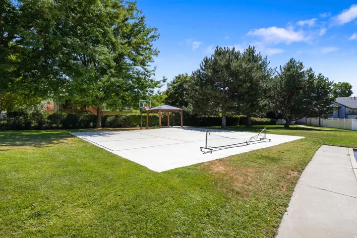 Concrete court with a basketball hoop, covered gazebo, and manicured lawn