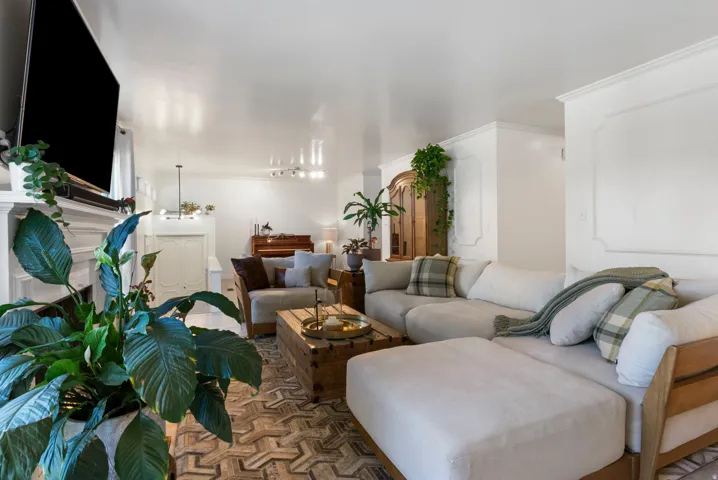 Living area featuring wood-finish flooring, a decorative fireplace with a mantel, and crown molding