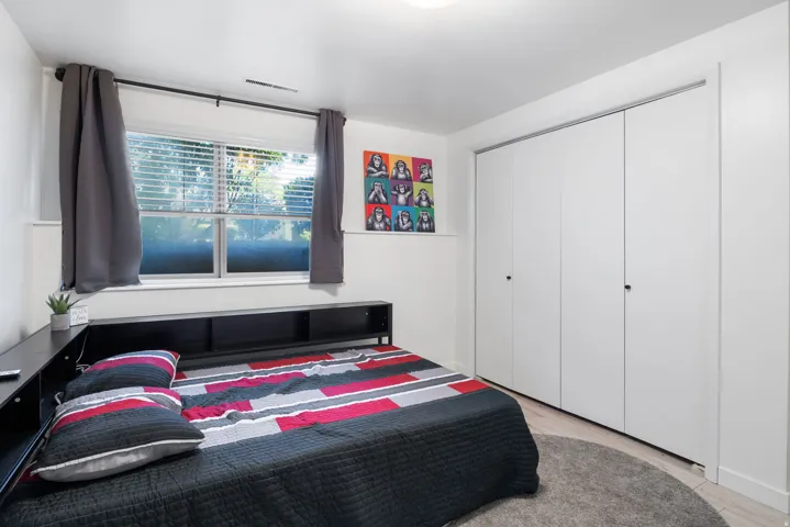 Window with blinds, flush-mount ceiling light, light wood-finish flooring, and bi-fold closet doors