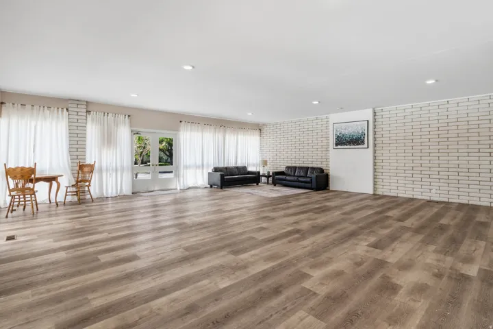 Expansive room with wood-finish flooring, white brick accent walls, recessed lighting, and glass paneled double doors