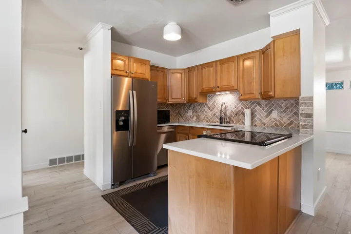 Kitchen featuring wood cabinetry, stainless steel appliances, herringbone tile backsplash, and light-toned countertops
