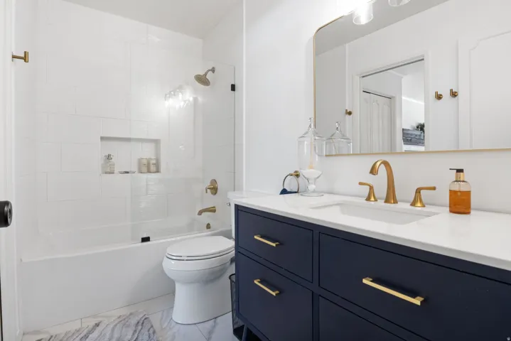White subway tile shower surround with recessed niche, glass shower panel, and brass-finish fixtures