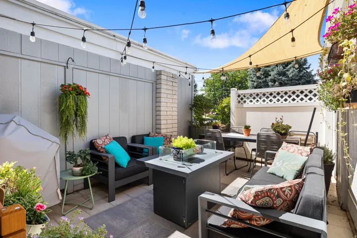 Paved patio area featuring string lights, a sunshade sail, slatted privacy walls, and a decorative lattice fence