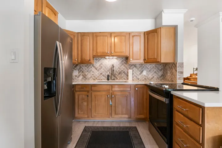 Stainless steel refrigerator, stainless steel range, wood-finish cabinetry, white countertops, and a herringbone tile backsplash