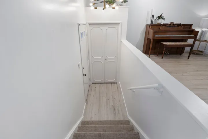 Carpeted staircase with white handrail, leading to a landing with wood-finish flooring