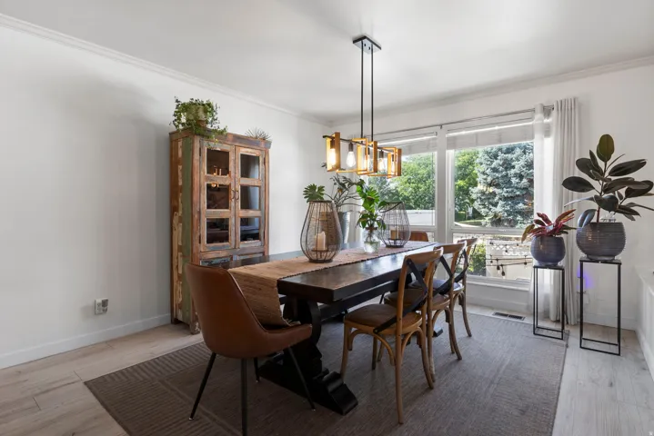 Spacious dining area featuring a linear pendant light fixture, wood-finish flooring, and large windows with outdoor scenery