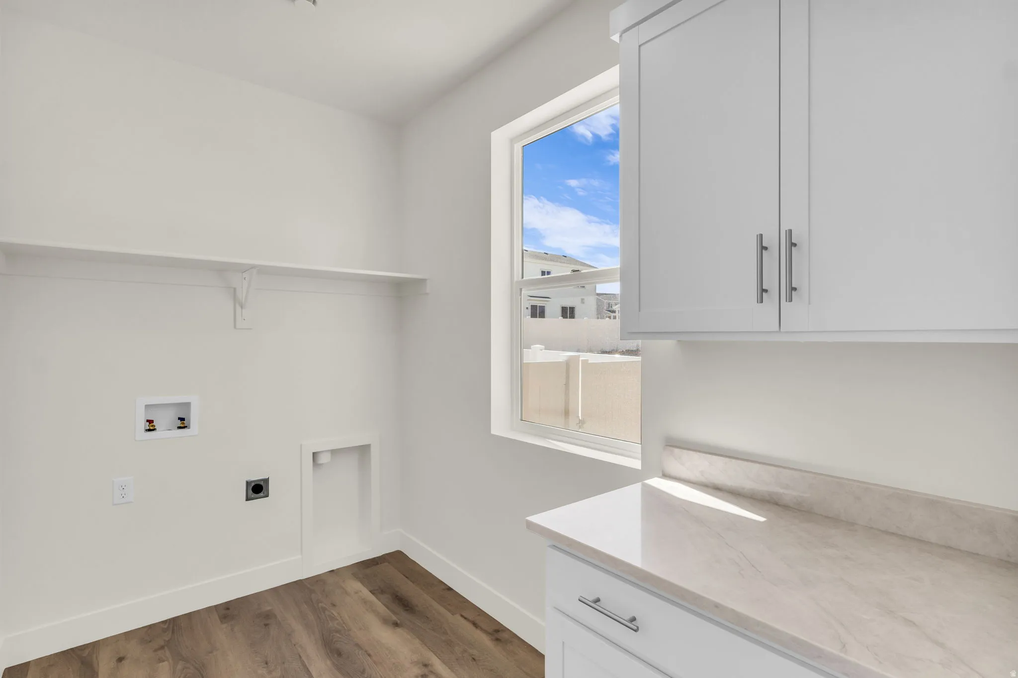 Laundry area featuring white cabinetry, a light-toned countertop, and wood-finish flooring