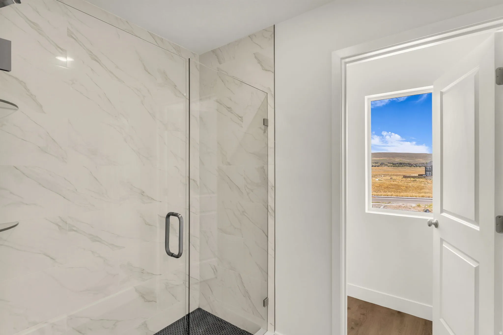 Glass-enclosed shower with full-height tile surround, black tile shower floor, and built-in corner shelving