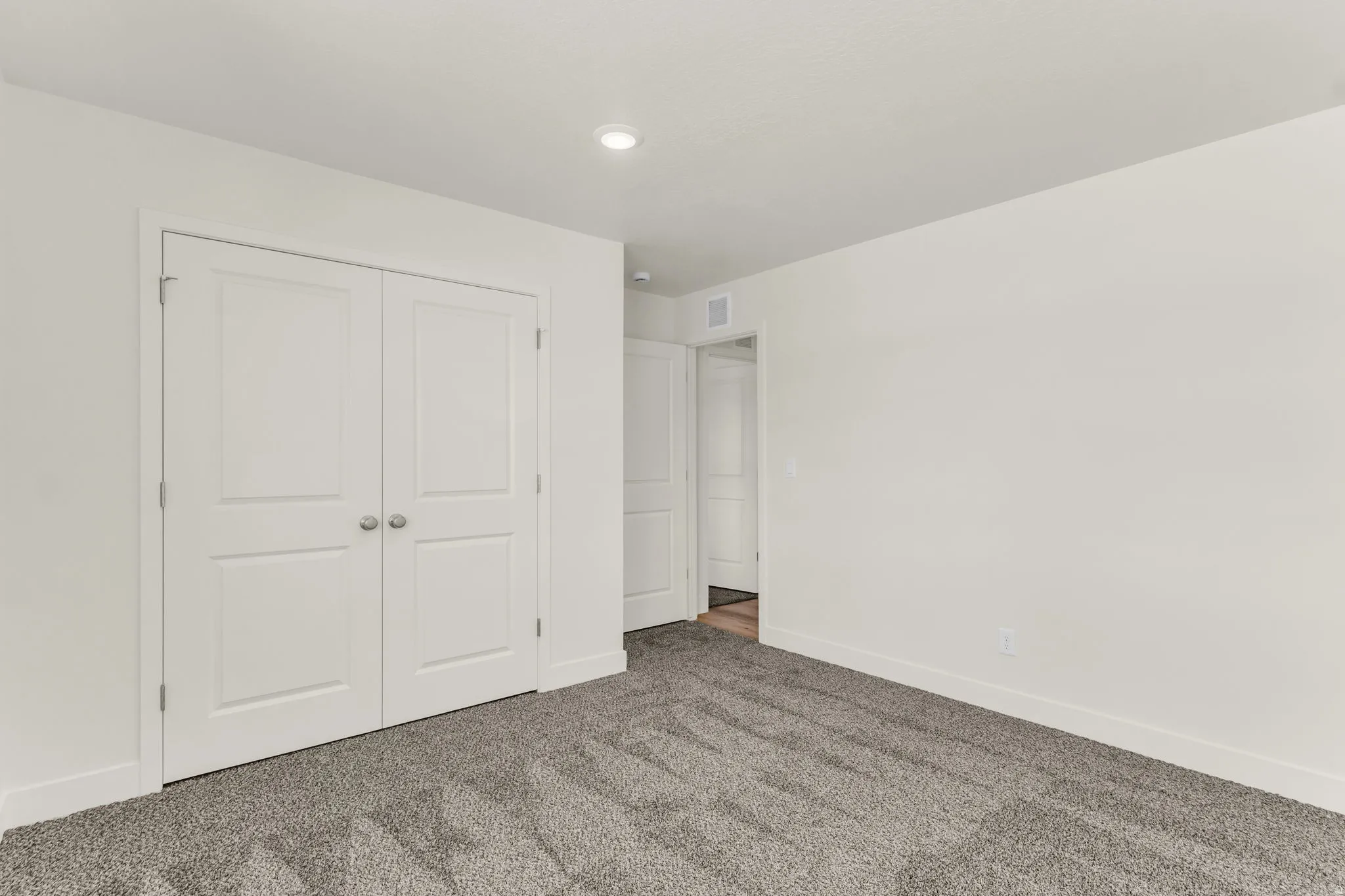 Recessed ceiling lighting, white walls, two-panel interior doors, gray carpet flooring, and white trim