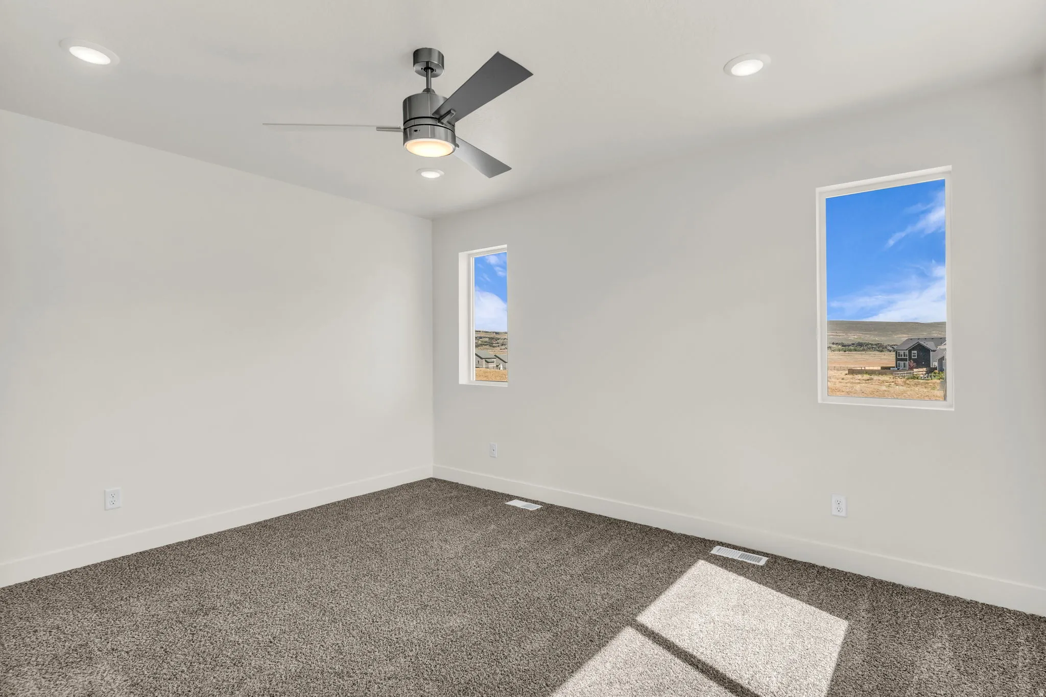 Recessed lighting, ceiling fan with integrated light, two vertical windows, and grey carpeting