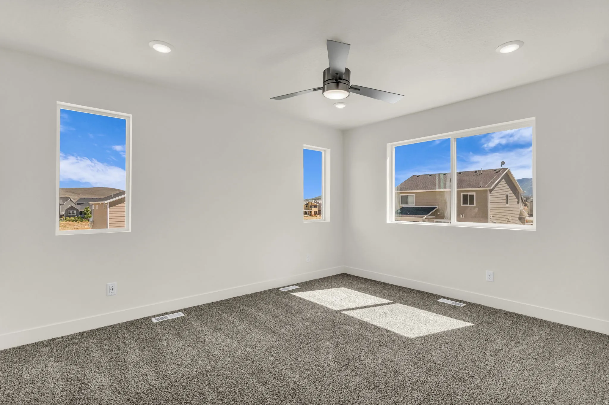 Recessed lighting, modern ceiling fan, multiple windows, white walls, and gray carpet
