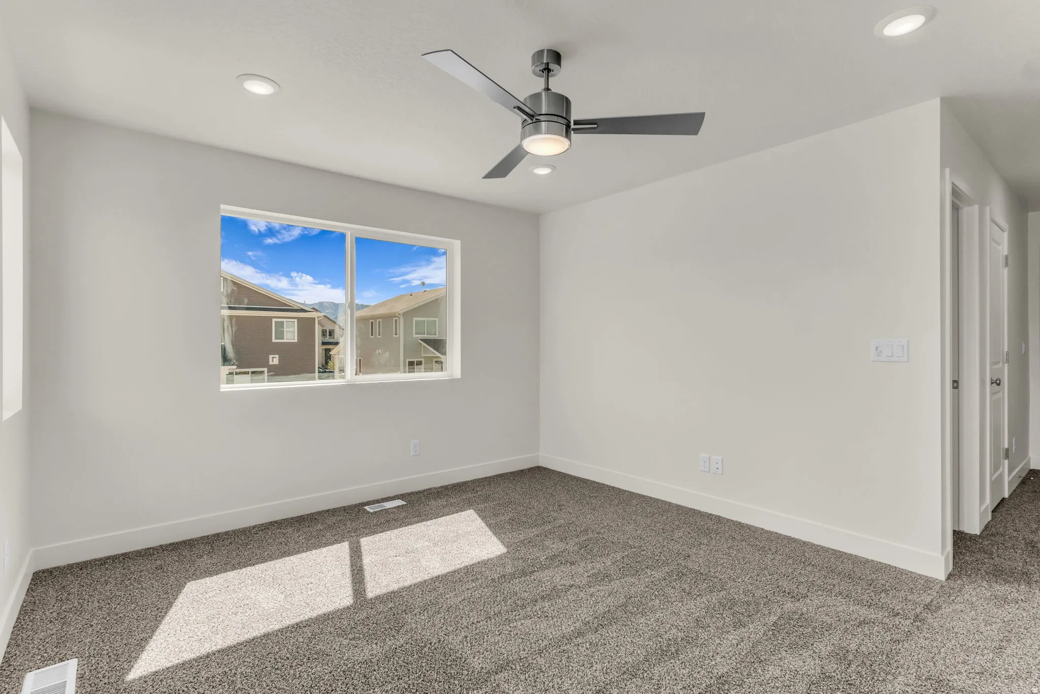 Spacious room featuring neutral carpeting, a large window, a modern ceiling fan with lighting, and recessed ceiling lights