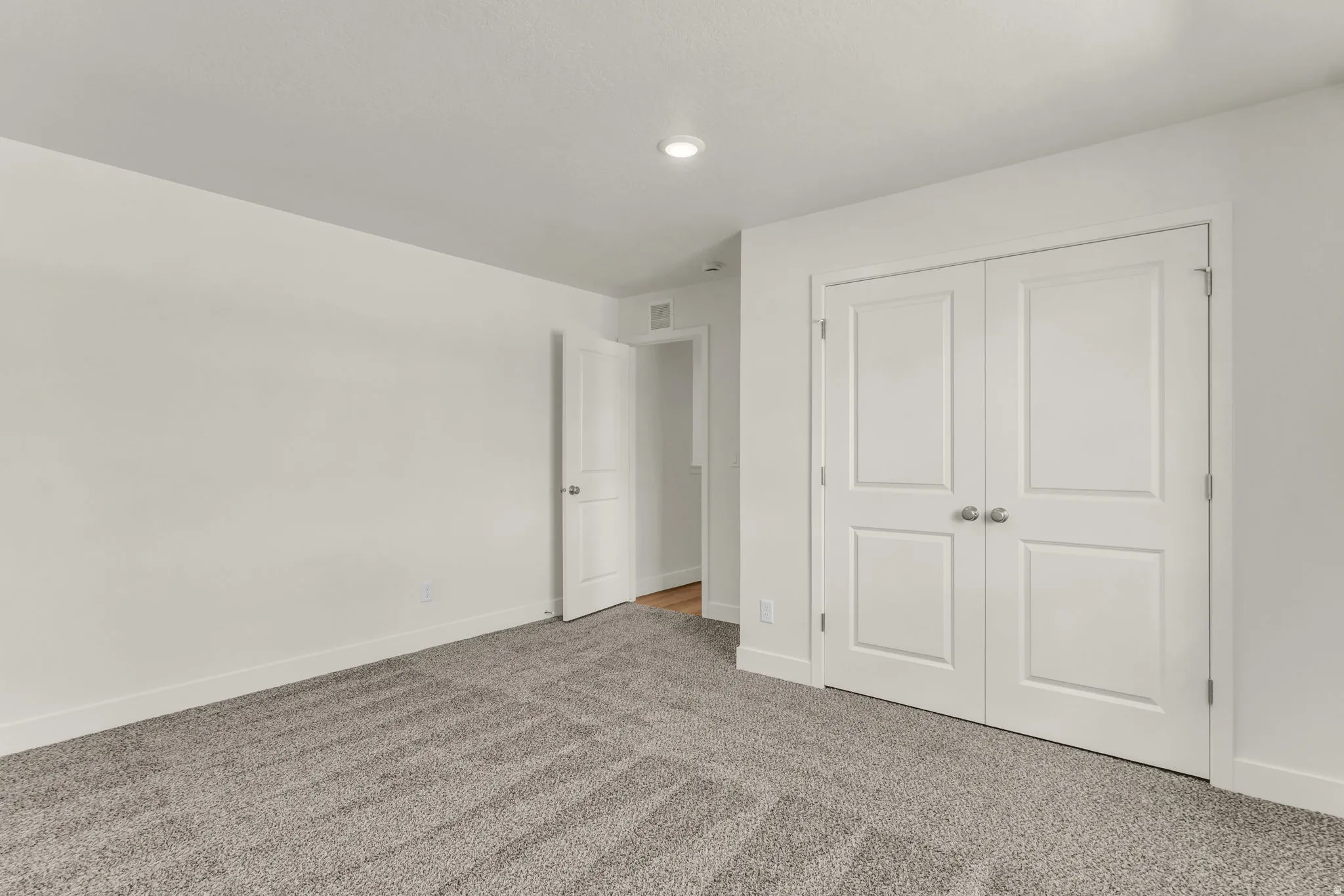 Wall-to-wall carpeting with a neutral finish, recessed lighting, and white bi-fold closet doors