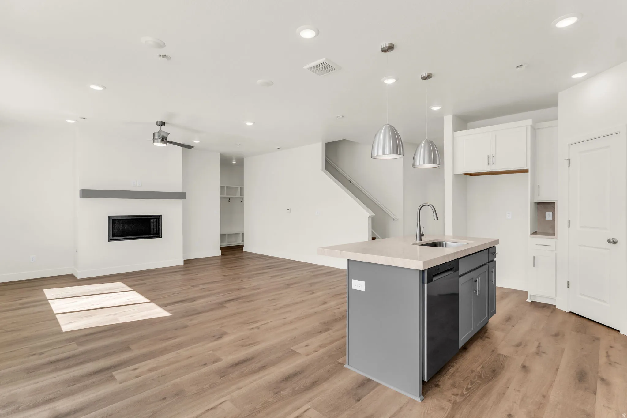 Open-concept living area featuring wood-finish flooring, a contemporary fireplace with a sleek mantel, and a kitchen island with a built-in sink and pendant lighting