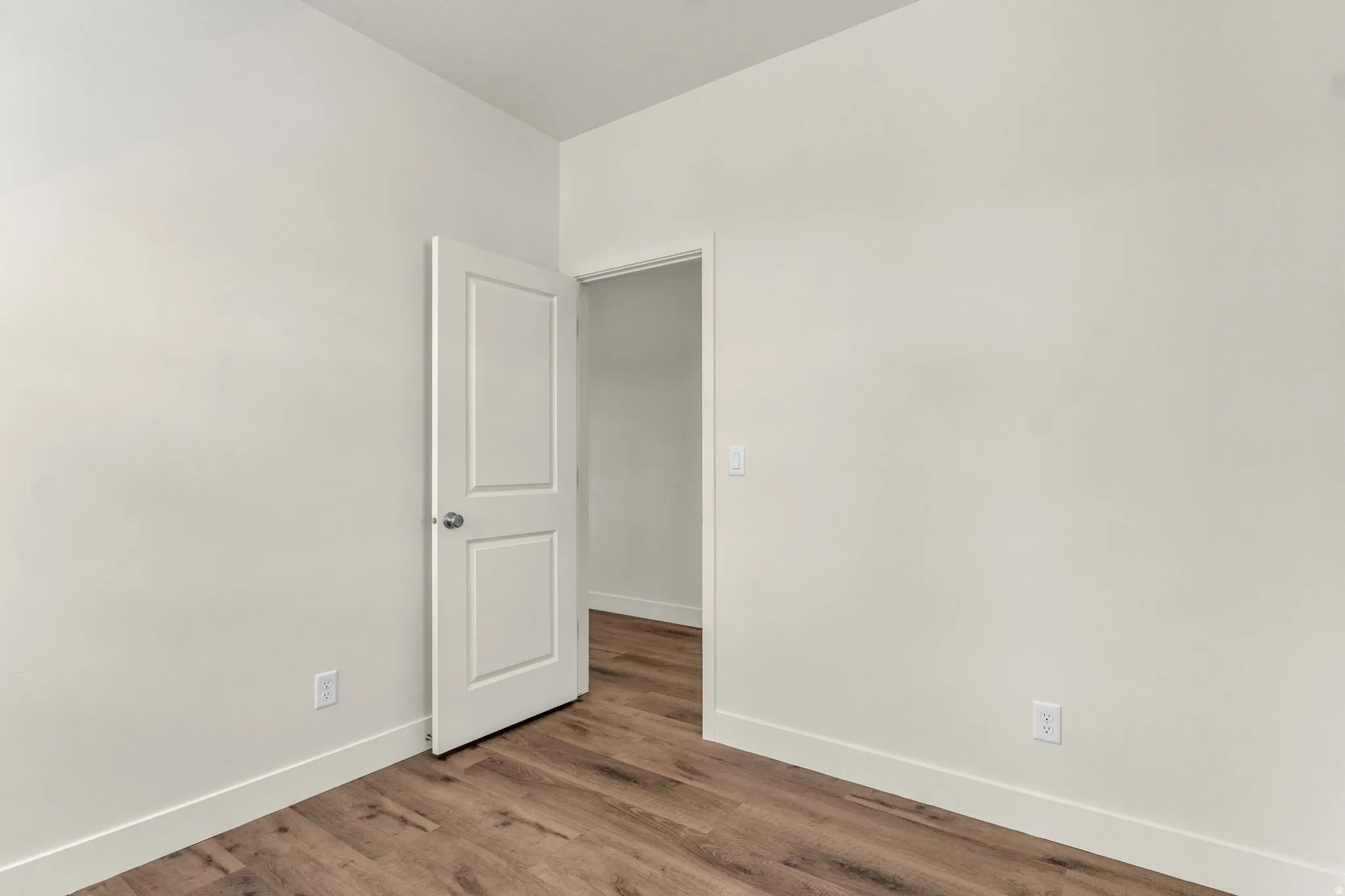Wood-finish flooring with white baseboards, light-toned walls, and a white interior door
