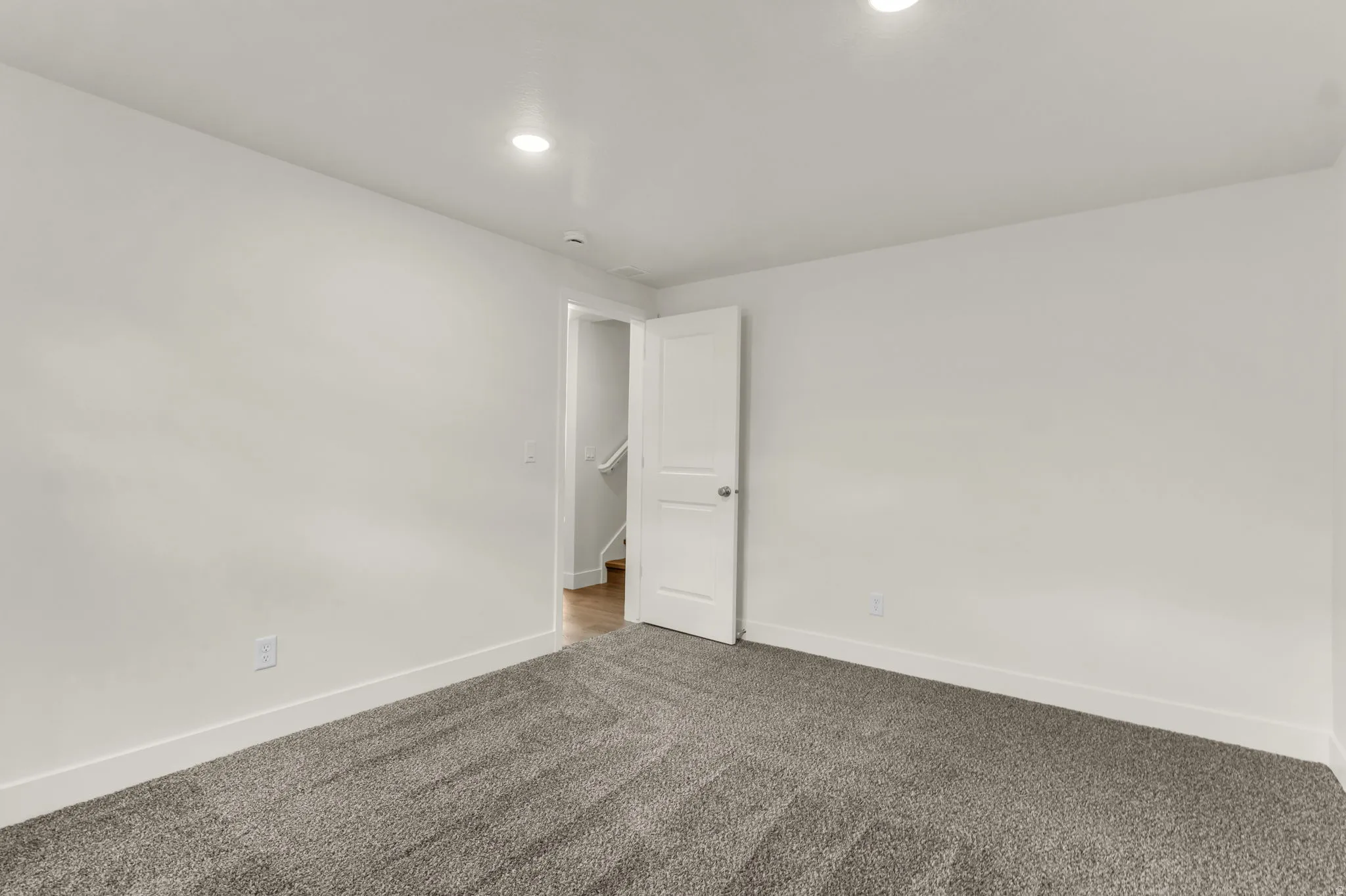 Recessed ceiling lighting, neutral wall paint, gray carpet flooring, white trim, and a white interior door