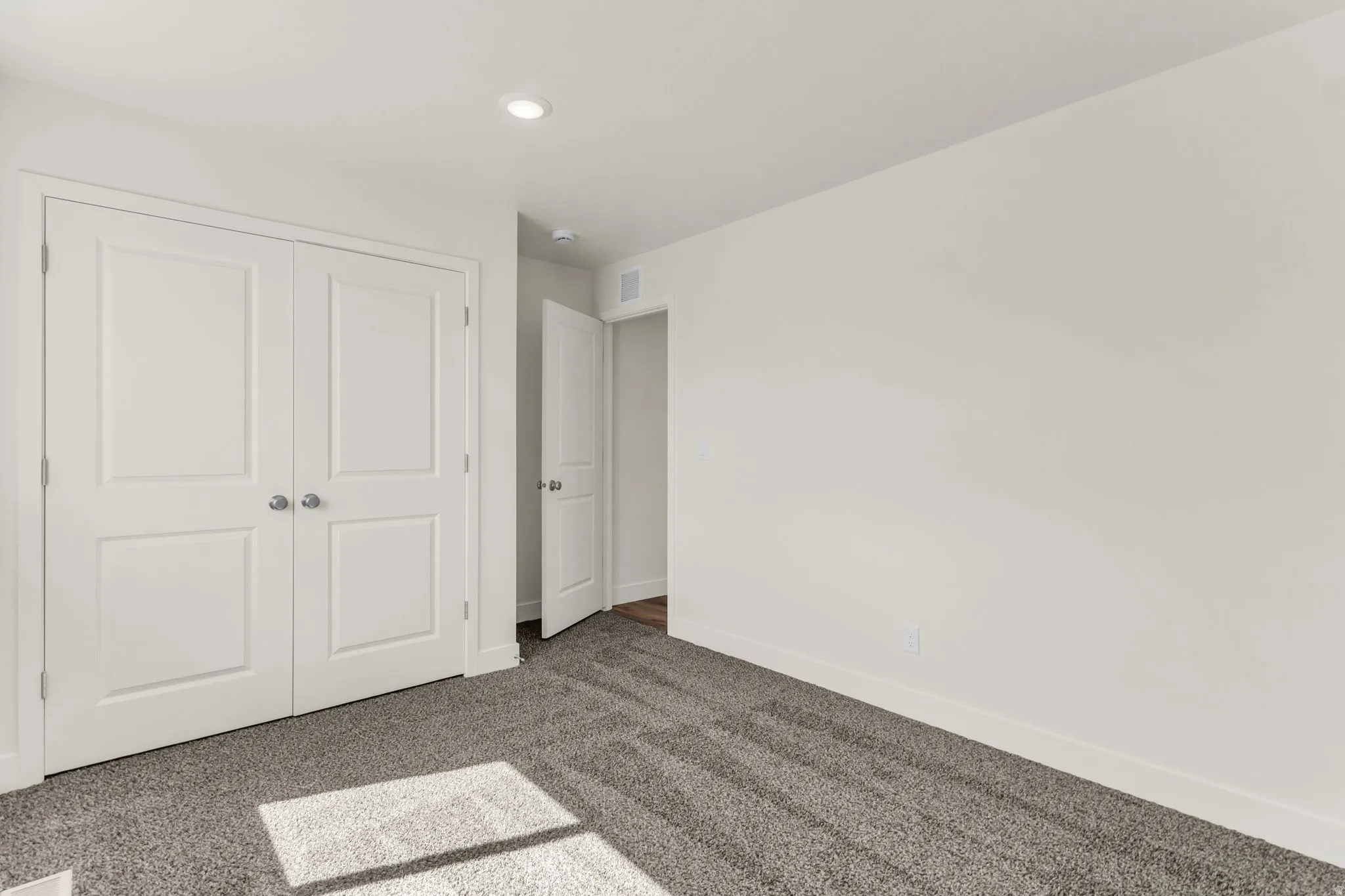 Recessed lighting illuminates neutral walls and gray carpet flooring