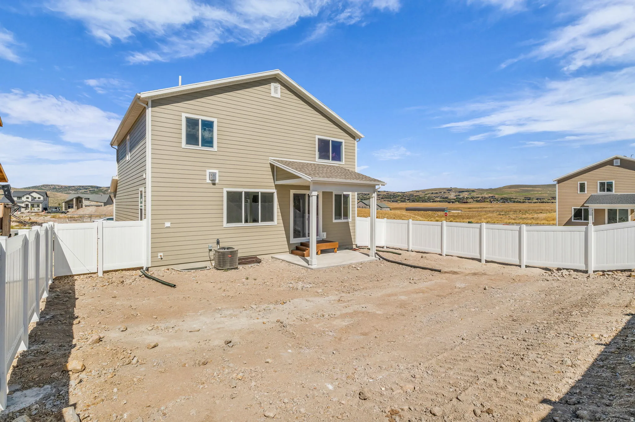 Rear exterior with beige siding, a covered patio, and white privacy fencing