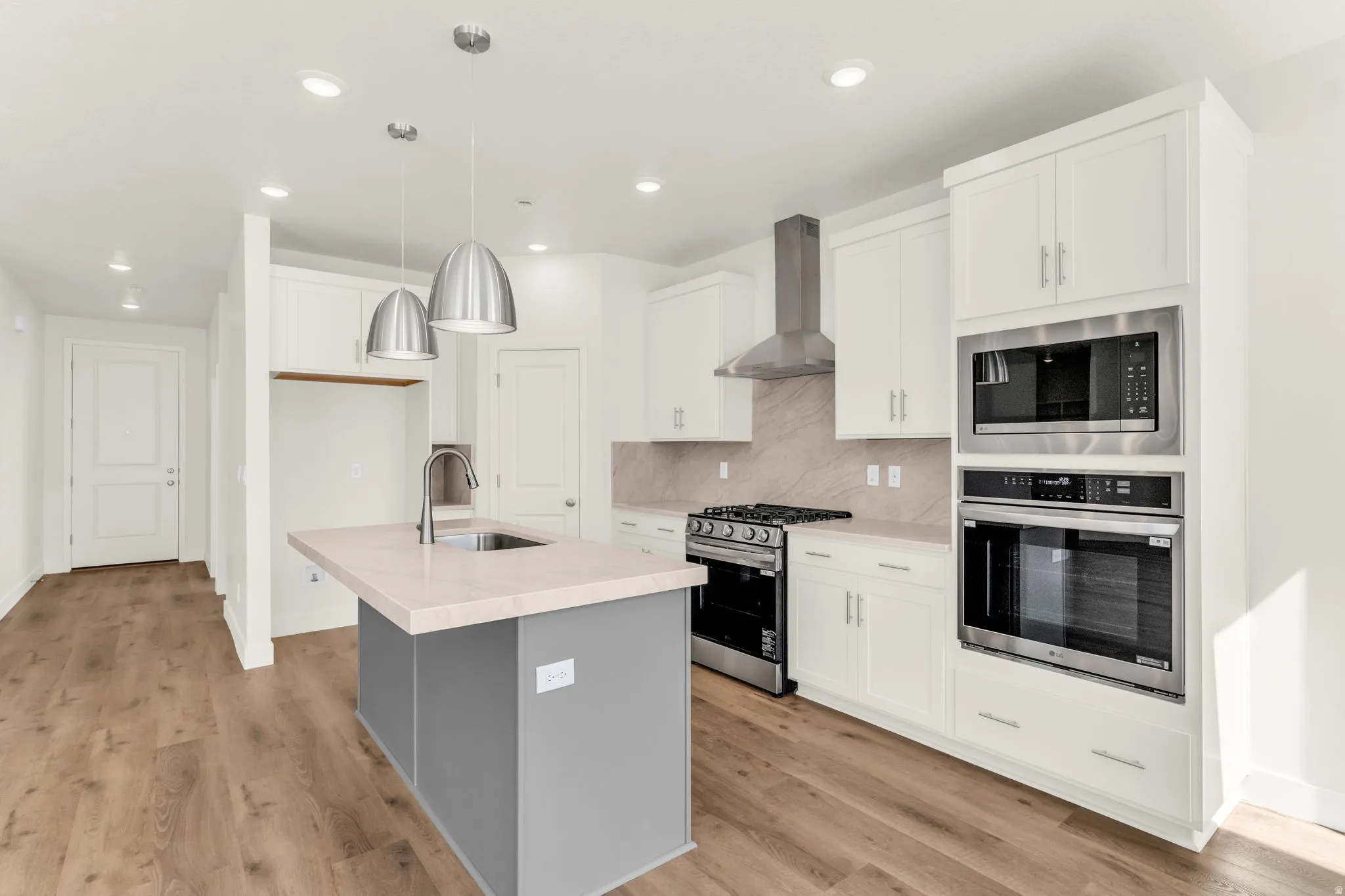 Kitchen with wood-finish flooring, white cabinetry, a gray kitchen island with a light-toned countertop, and stainless steel appliances